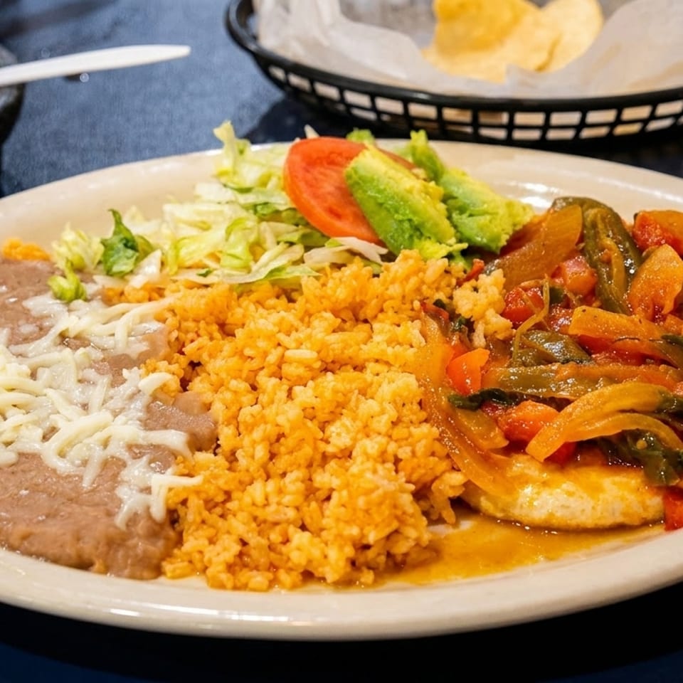 A Mexican dinner plate with rice, refried beans, chicken with vegetables, and a side salad.