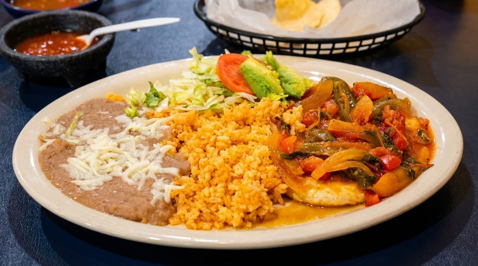 A Mexican dinner plate with rice, refried beans, chicken with vegetables, and a side salad.