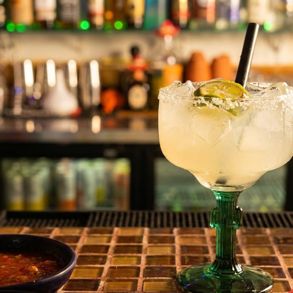 Margarita with lime and salt rim, salsa, and shredded lettuce on a bar counter.