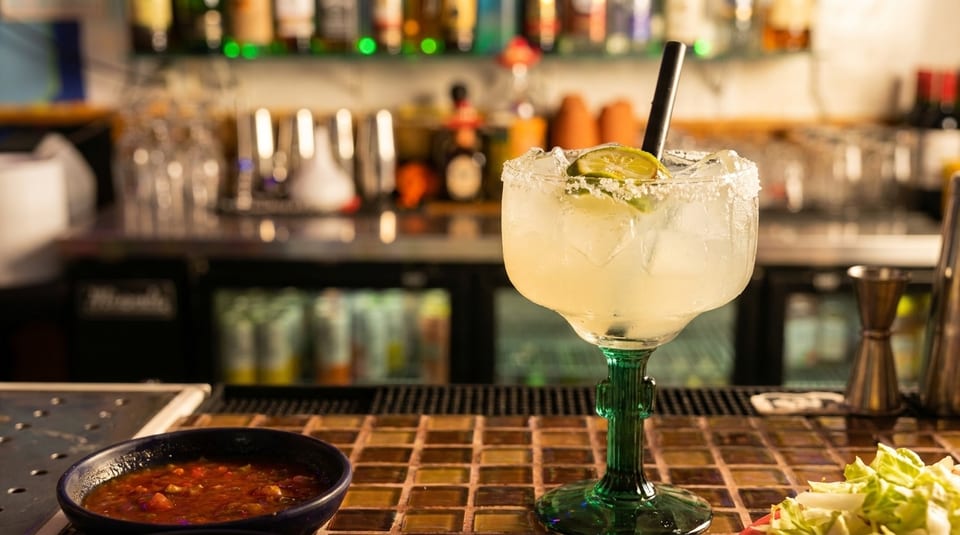 Margarita with lime and salt rim, salsa, and shredded lettuce on a bar counter.